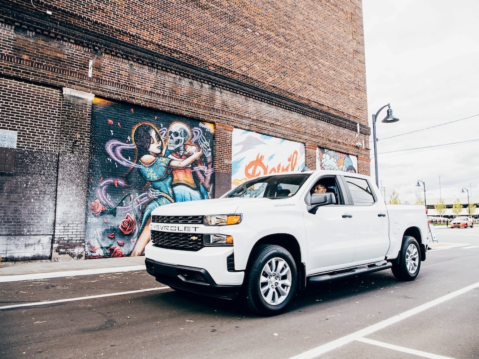 Freddy Diaz in a white Silverado on a Detroit street next to one of Freddy’s colorful murals on the side of a brick building.