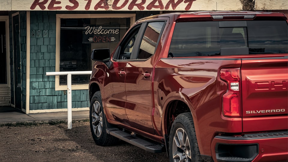 A red Chevy Silverado seen from the back, parked in front of a building with the word “Restaurant” above the door.