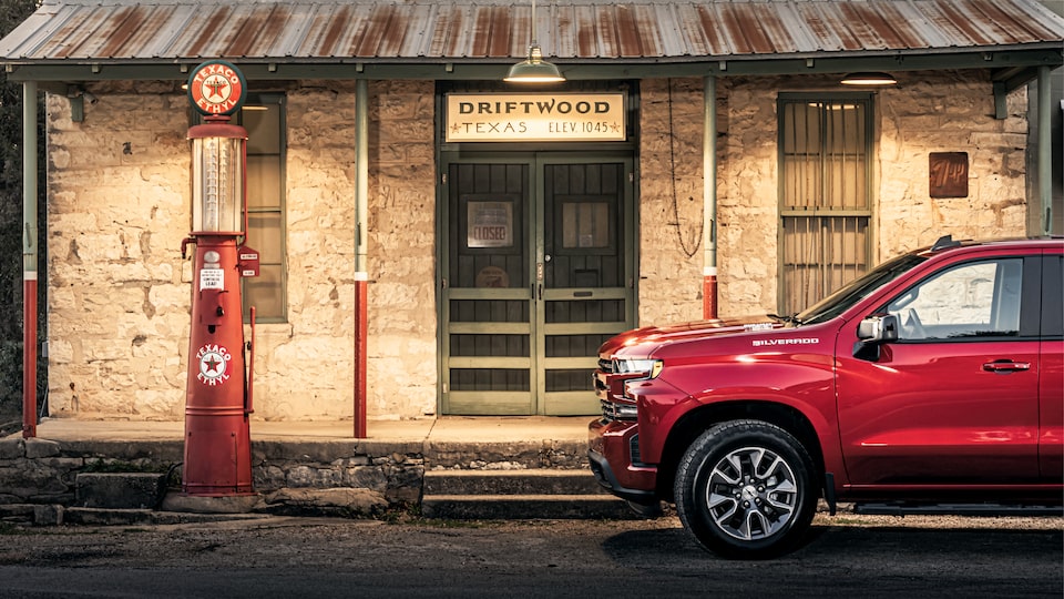 A red Chevy Silverado parked in front of the former Driftwood Country Store in Driftwood, Texas. An old-time red gas pump is in front of the store.