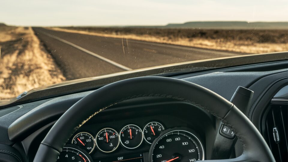 A straight strip of two-lane highway stretches into the distance, seen from over the steering wheel of a Chevy Silverado.
