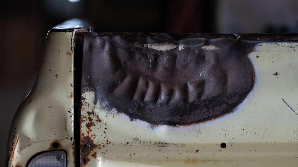 A burned-out area on the tailgate of an old white Chevy pickup.