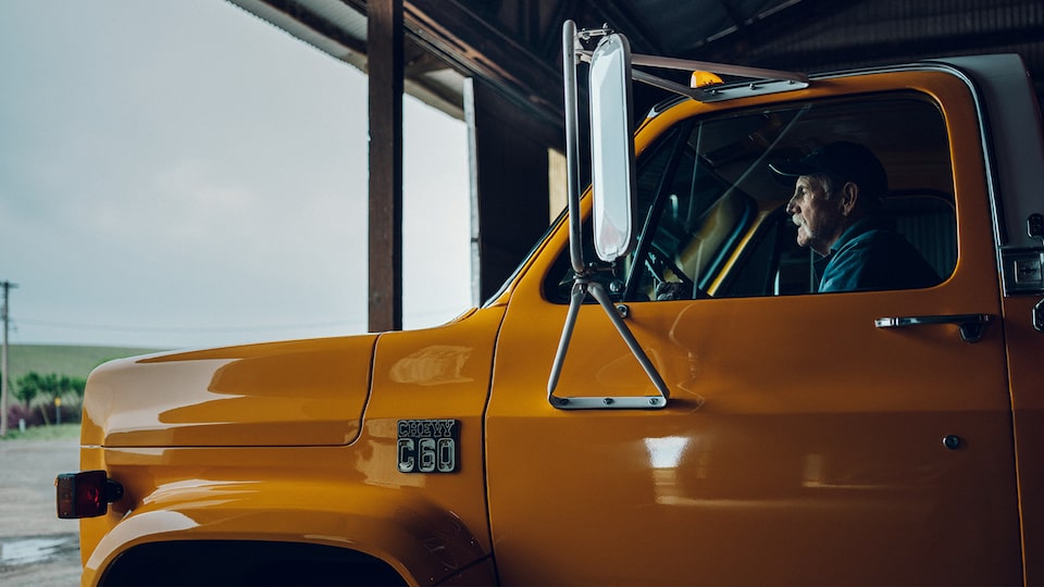 A man in an old yellow Chevy C60 truck drives out of a building.