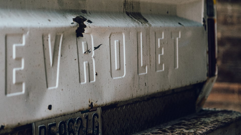 The dented and rusted tailgate of an old Chevy pickup, with the Chevrolet name across the back.