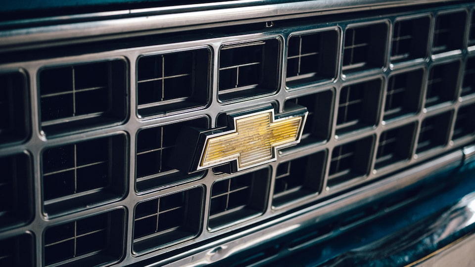 A close-up of the Chevy bowtie emblem on the grille of an old Chevy truck.