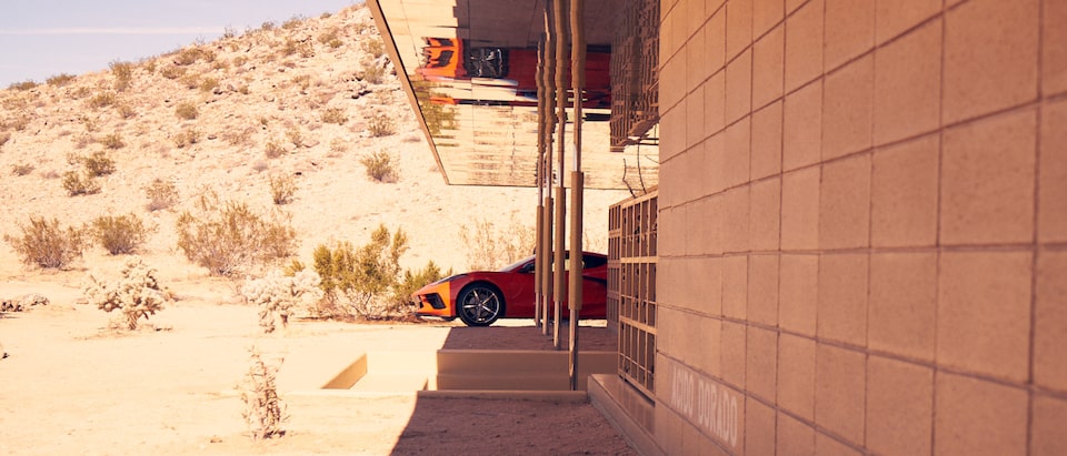 A Torch Red 2020 Corvette is parked in the shade next to a contemporary home in the desert Southwest, with a sun-baked desert landscape in the background.