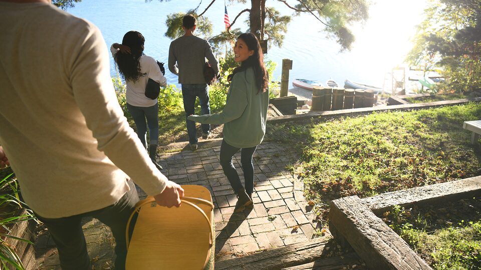 A woman with a picnic basket walks down the stairs with three friends toward Lake Wandawega.