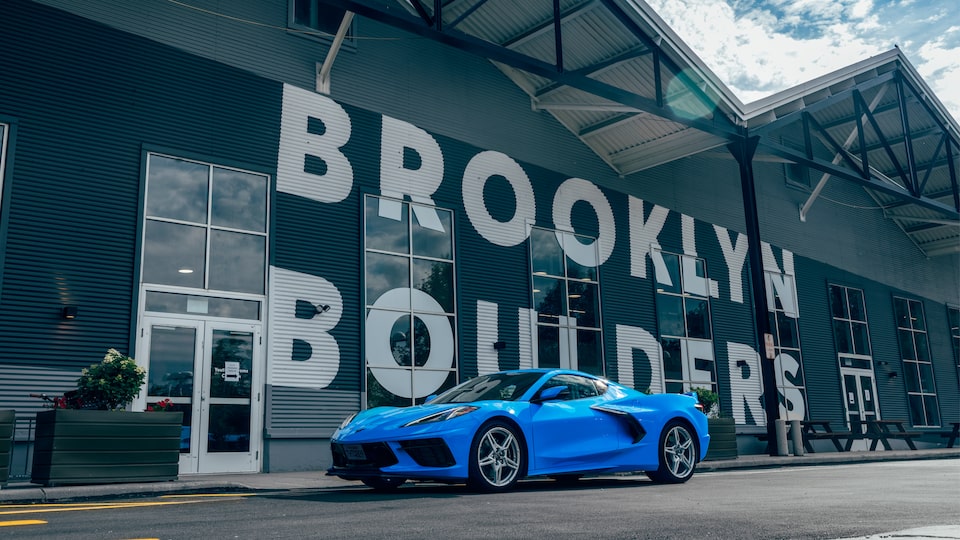 A bright blue 2020 Corvette sits on the street in front of a rock climbing gym with the name "Brooklyn Boulders" in huge white letters on the front of the building.