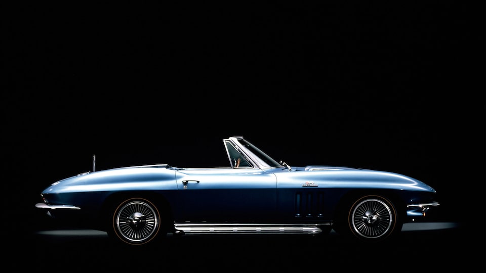 A Generation 2 (C2, 1963-1967) blue Corvette Convertible with the top down seen from the side against a black background.
