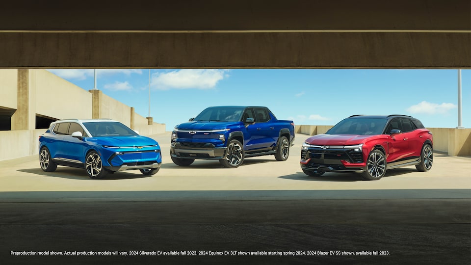 A blue Equinox EV, a blue Silverado EV, and a red Blazer EV are parked together on the open top level of a parking garage.