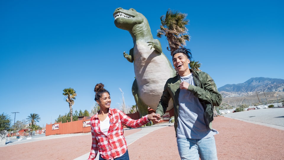 A couple holding hands in front of one of the Cabazon Dinosaurs.