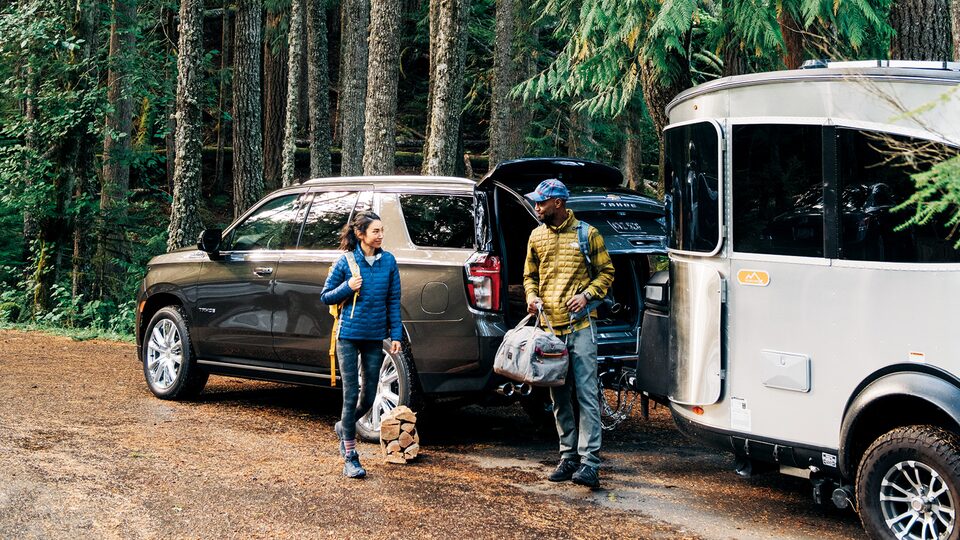 A black 2021 Chevy Tahoe pulls an Airstream Basecamp X trailer through a wooded area.