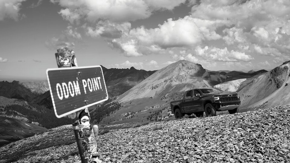 A Silverado ZR2 sits on a gravel road above the treeline in the Colorado mountains. A sign that reads "Odom Point" stands off to the side.