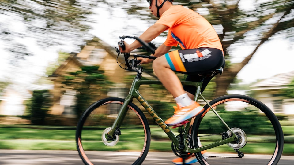 Chris Nikic in training, riding his bike through a neighborhood that is blurred behind him.