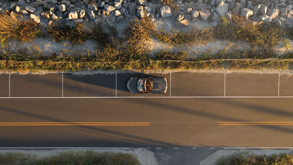 A Corvette convertible is seen from directly above on a coastal highway.