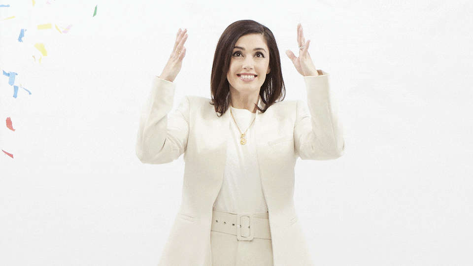 An animation showing Jennifer Widrick dressed in white and standing in front of a white background while she throws handfuls of colorful confetti into the air.