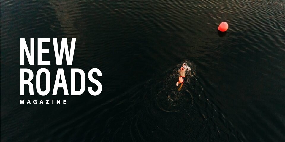 Chris Nikic swims in a lake as part of his Ironman training. The words “New Roads Magazine” appear over the photo.