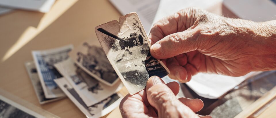 George Patton Waters' hands holding an old picture of a tank, with other old photos on the table below.