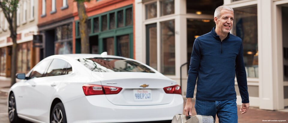 Mike Lucey walking away from his Chevrolet Malibu, carrying his guitar case.