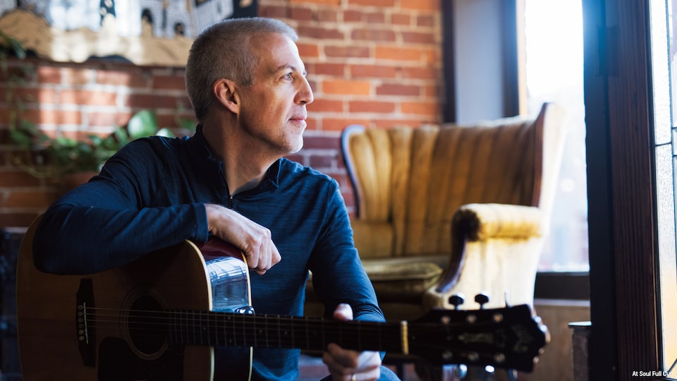 Mike Lucey sitting in a café with his guitar.