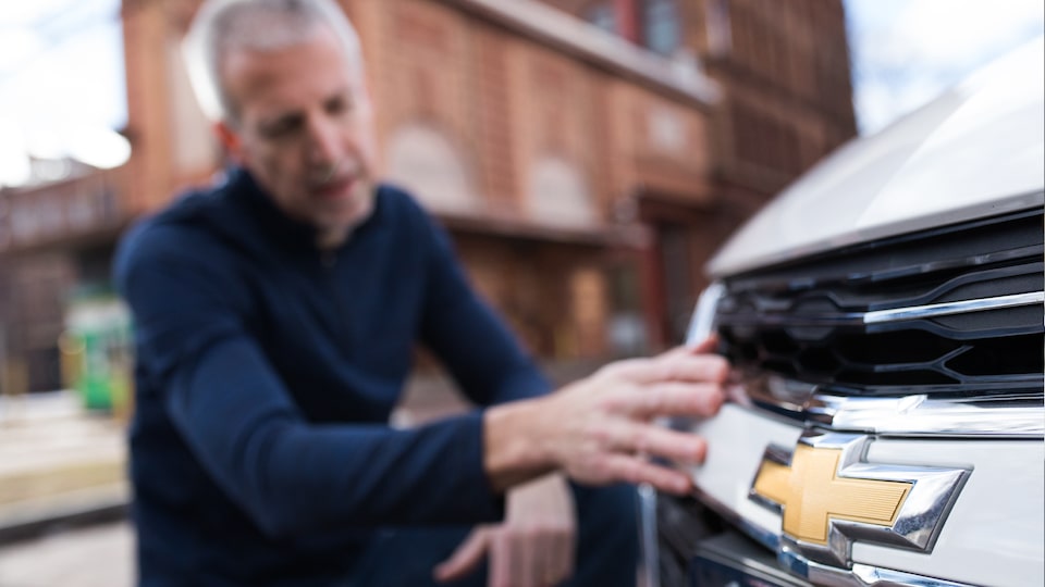 Mike Lucey resting his hand near the Chevrolet bow tie on the front of his Malibu.