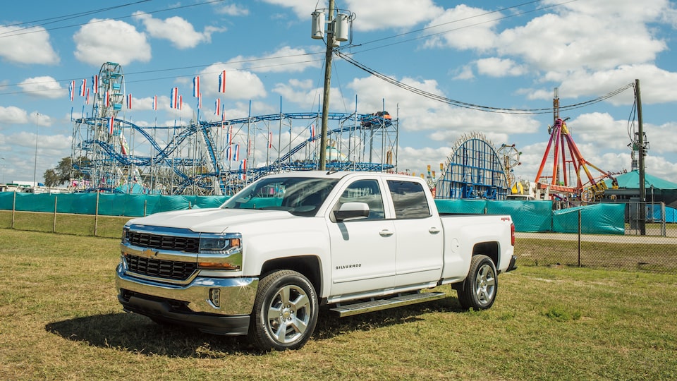 Una Chevy Silverado estacionada con una montaña rusa de la feria estatal en el fondo.