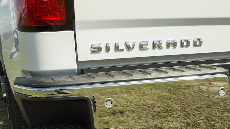 Primer plano del emblema de la Silverado sobre la puerta trasera de una camioneta blanca.