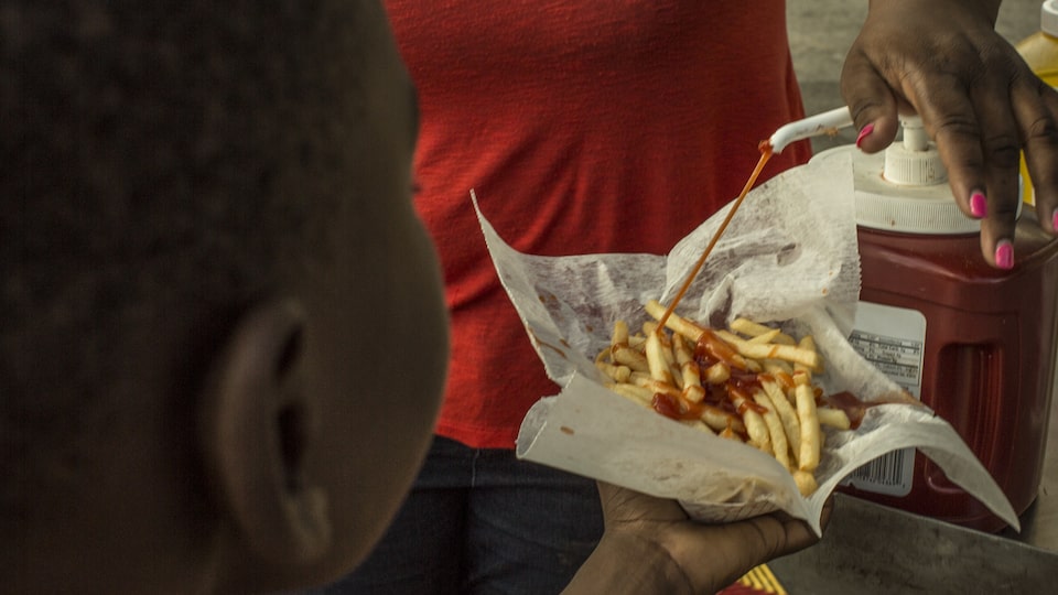 Un niño colocando ketchup en sobre unas patatas fritas muy calientes.