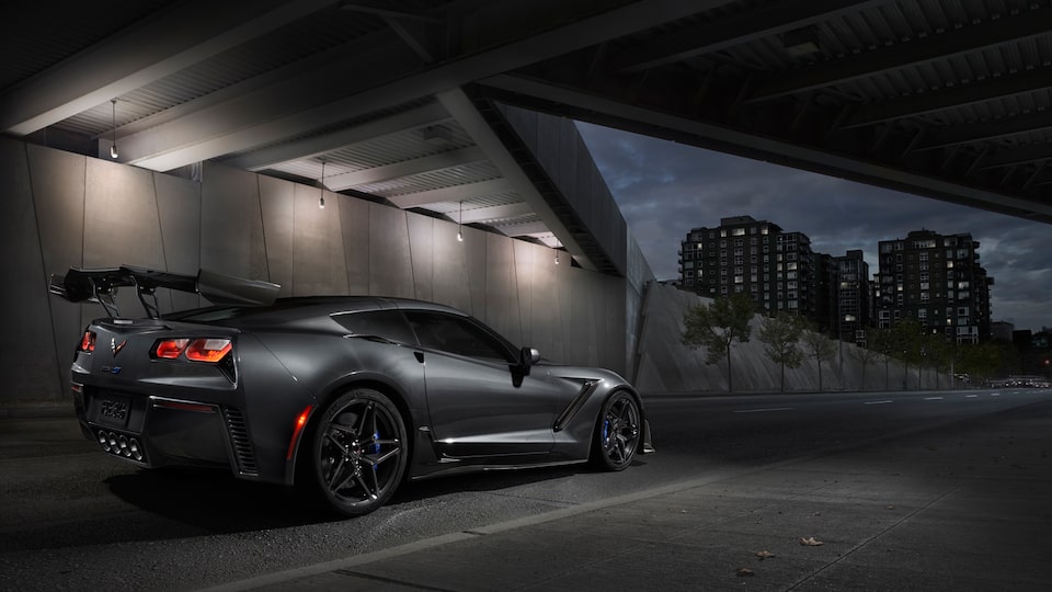 A black 2019 Corvette ZR1 with the available ZTK Performance Package seen from the right rear under a highway overpass, with red taillights glowing.