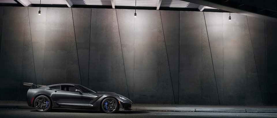 A black 2019 Corvette ZR1 with the available ZTK Performance Package seen from the side in semi-darkness against the concrete wall of a highway overpass.