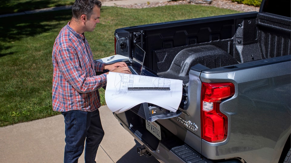 A person uses a laptop on the work surface provided by the Silverado Multi-Flex tailgate configured as a type of standing desk.