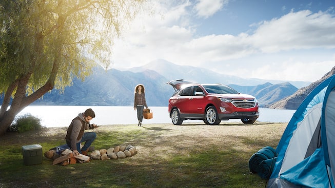 A couple sets up their lakeside camping site, taking gear out of their Chevrolet Equinox.
