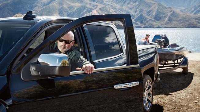 A man uses a Chevy Silverado to back a boat on a trailer into a boat launch at the lake.
