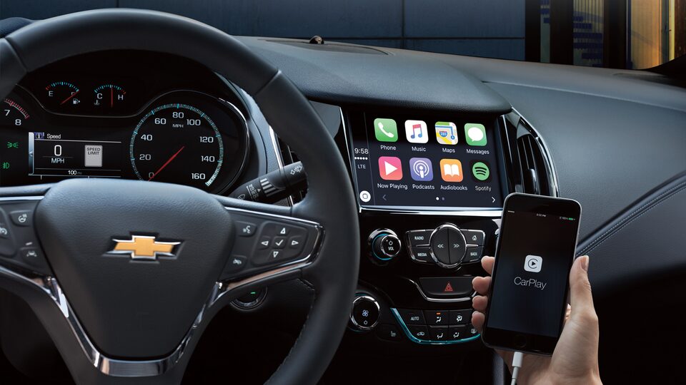 A hand holding a phone displaying the Apple CarPlay interface.