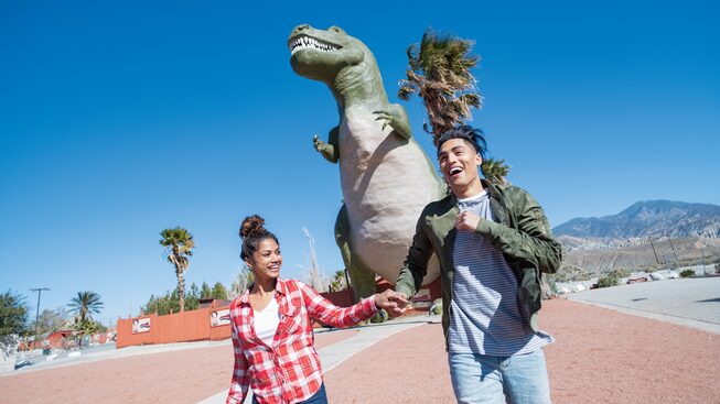 Una pareja tomada de las manos frente a uno de los Cabazon Dinosaurs.