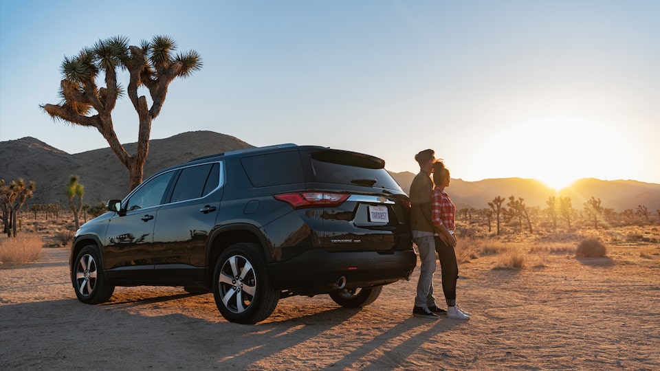 A couple standing behind the Chevrolet Traverse as the sun sets.