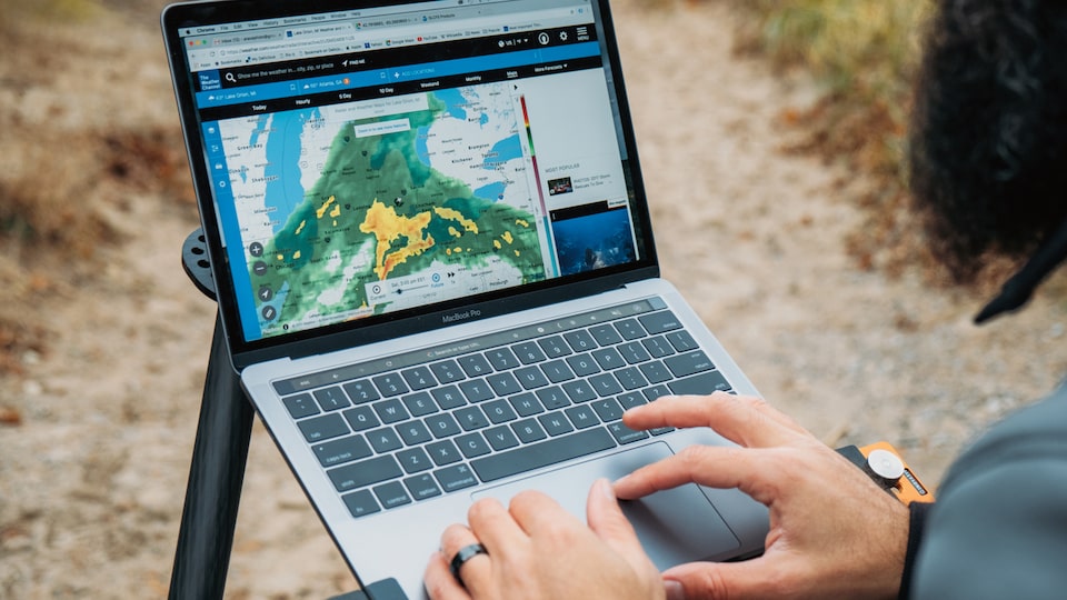 Chris Arace looking at a weather map on his laptop, which is set on a stand on a beach.