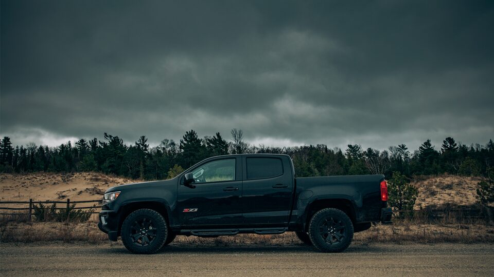 A black Chevy Colorado Z71 Crew Cab with the Midnight Edition package seen from the side in front of Lake Michigan sand dunes.