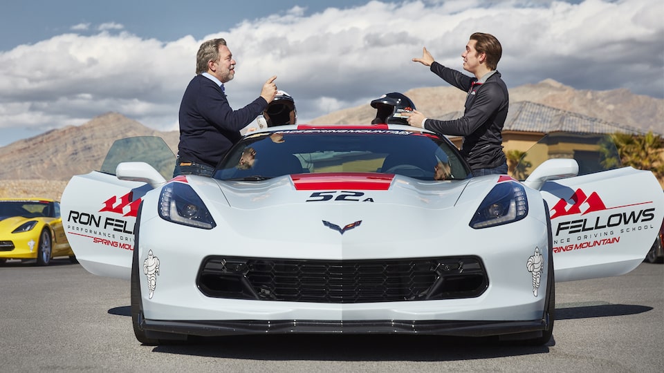Students stand and talk on either side of a white Corvette.