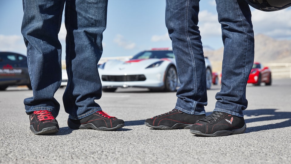 Two students feet as they stand on the track, with Corvettes behind them.