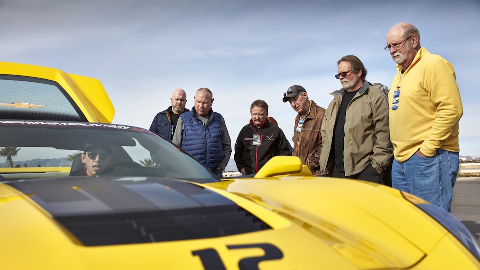 Students stand and admire a yellow Corvette.