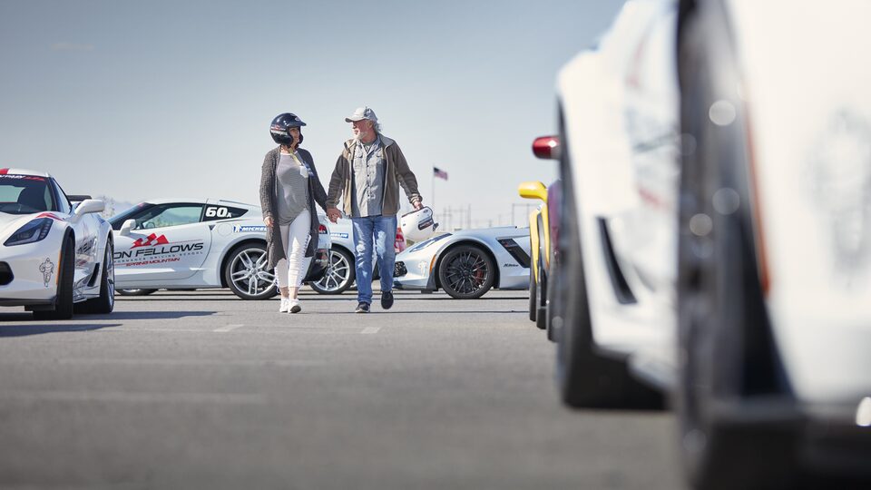 Two students talk as they walk past white Corvettes.
