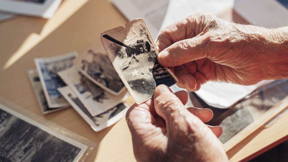 George Patton Waters' hands holding an old picture of a tank, with other old photos on the table below.