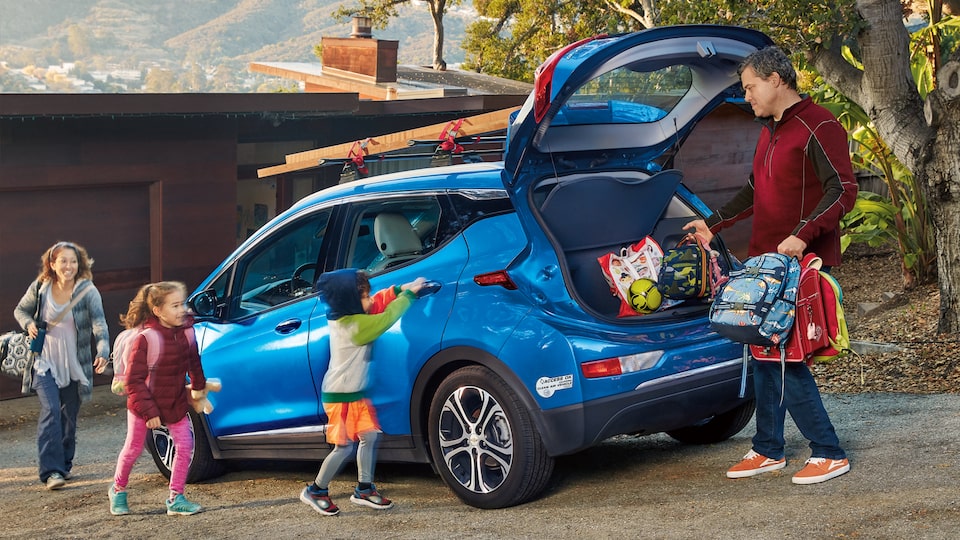 Ethan Stock junto a su esposa y dos hijos cargando cosas en la parte trasera de su Chevy Bolt EV 2017 color Azul.