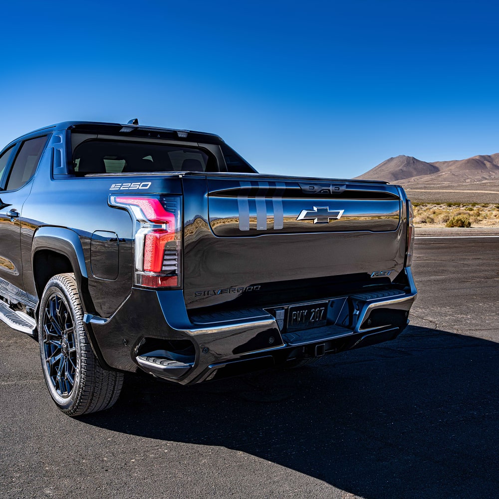A Rear Angled View of a Black Chevrolet Truck Parked on a Road with Mountains in the Background.