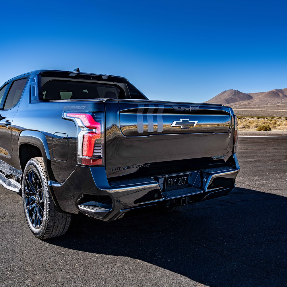 A Rear Angled View of a Black Chevrolet Truck Parked on a Road with Mountains in the Background.