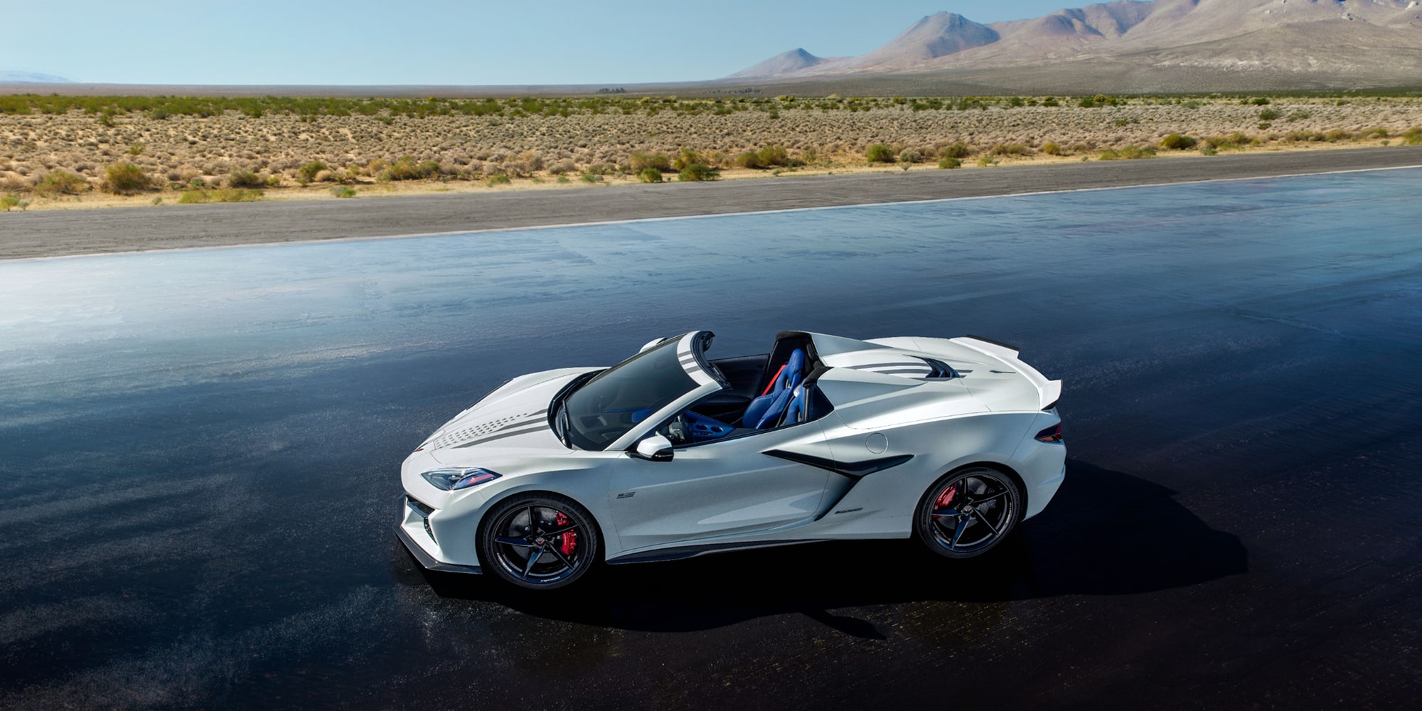 A White Chevrolet Corvette E-Ray Stars and Steel Convertible with Blue Interior on a Dark Asphalt Road.