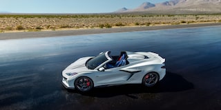 A White Chevrolet Corvette E-Ray Stars and Steel Convertible with Blue Interior on a Dark Asphalt Road.