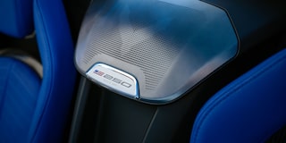 A Close-Up View Of A Chevrolet Interior Showcasing A Silver America250 Badge Integrated Into A Textured Speaker Cover Between Blue Leather Sport Seats.