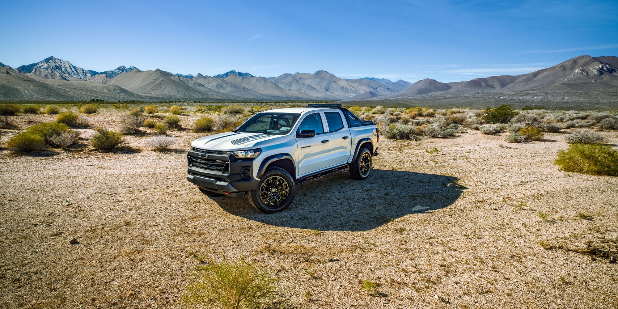 A White Chevrolet Colorado Special Edition Truck Standing on a Dirt Road with Mountains in the Background.