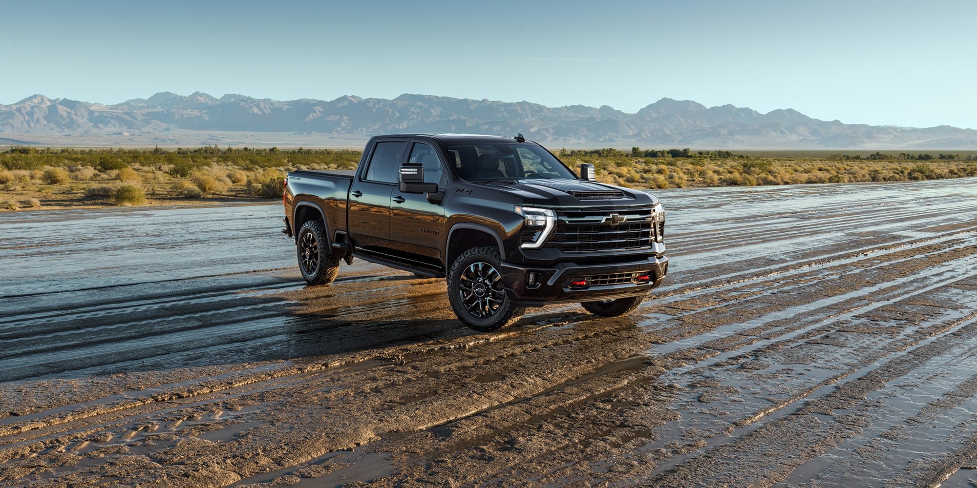 A White Chevrolet Silverado HD Stars and Steel Edition Truck on a Wet Dirt Road with Mountains.